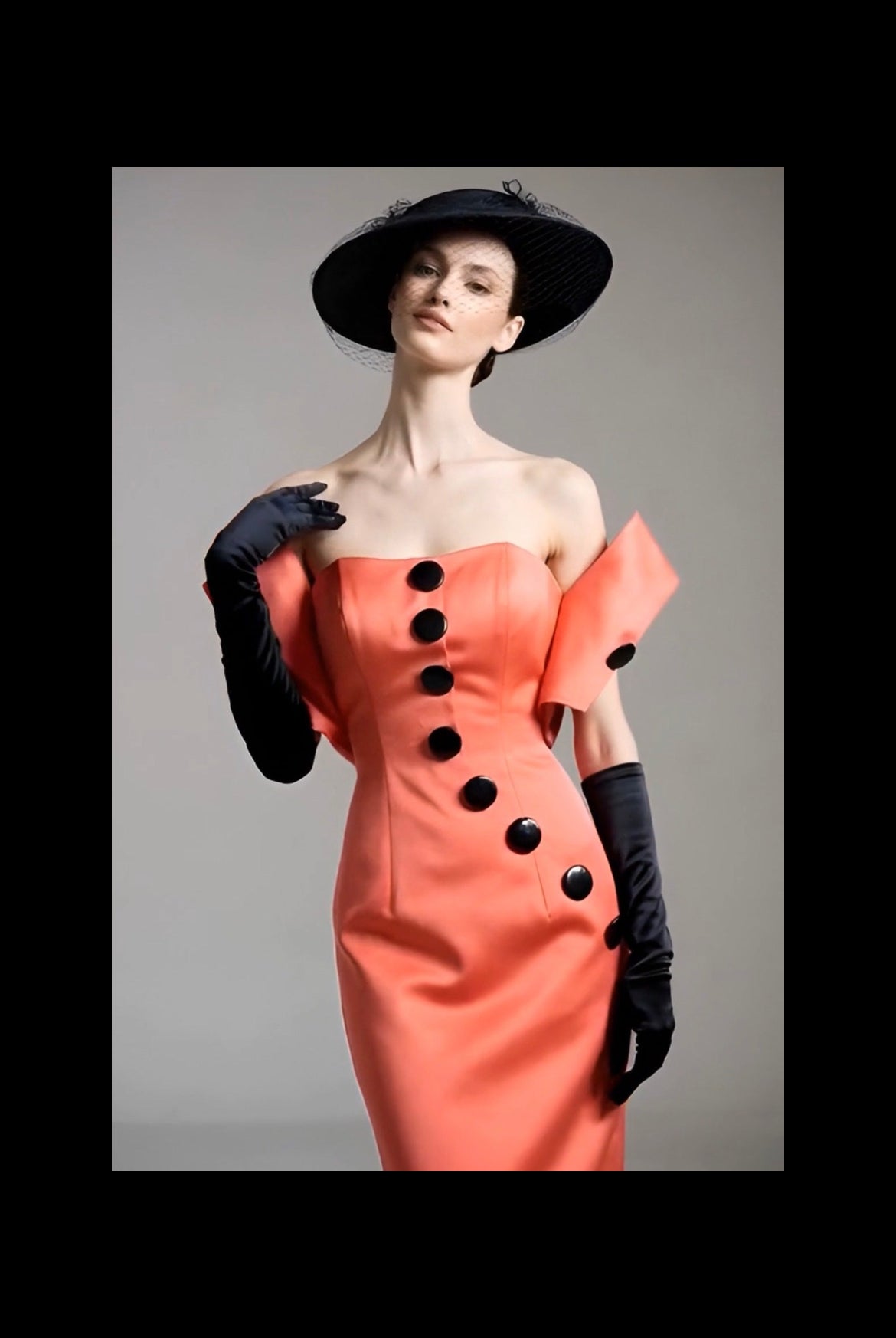 Woman wearing a peach dress with black buttons and black gloves against a gray background